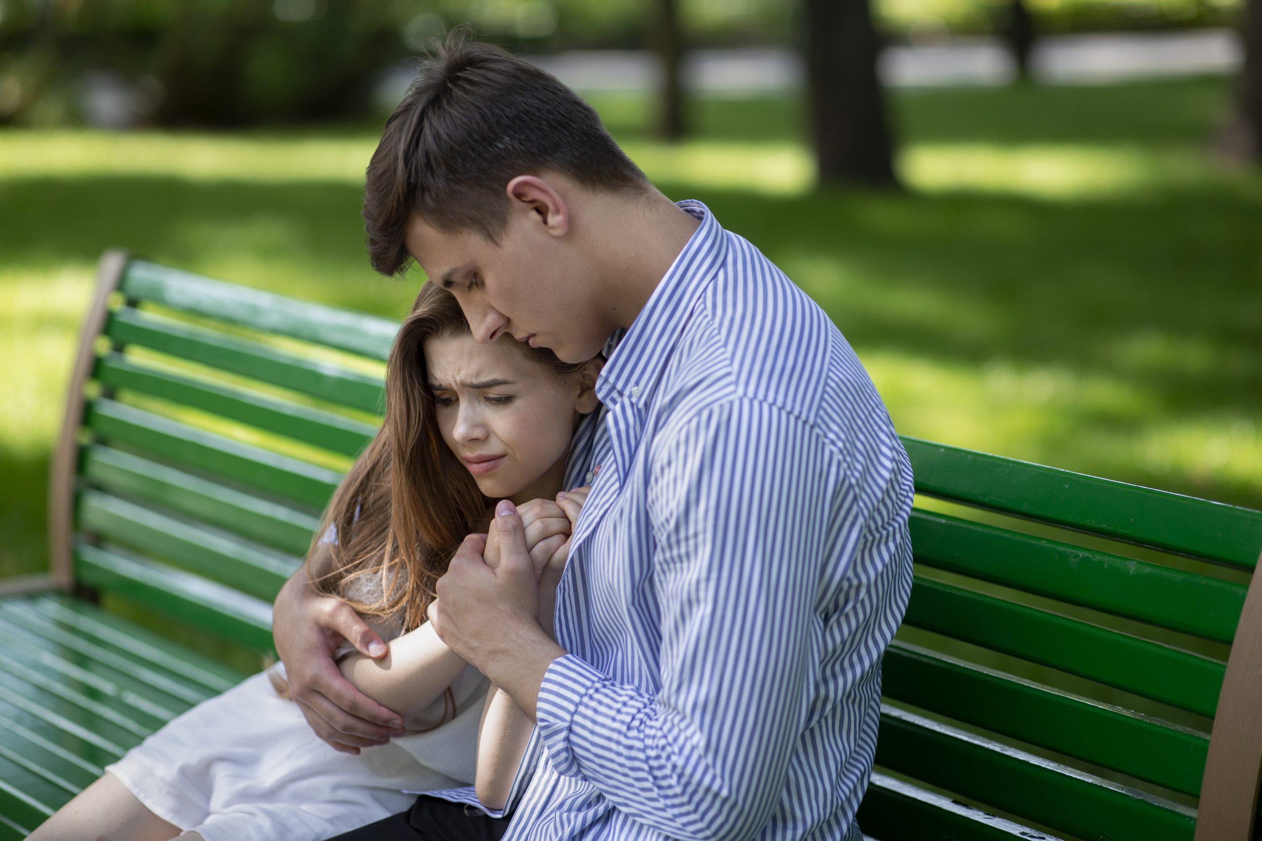 Young guy consoling his upset girlfriend on bench at urban park