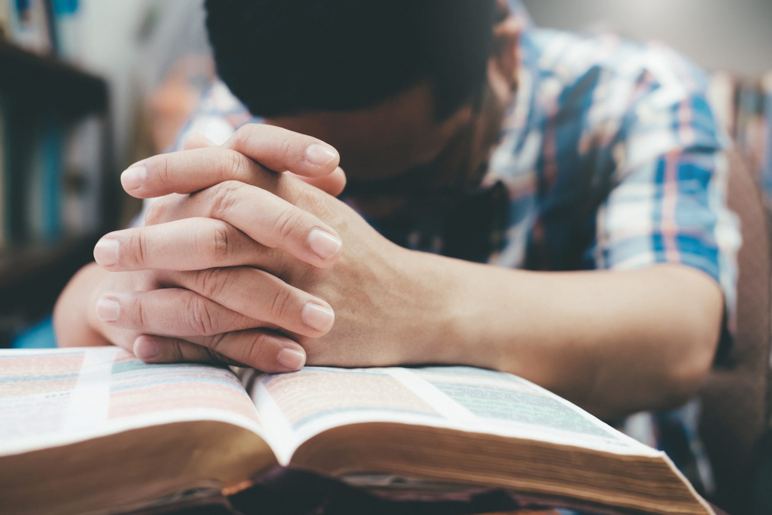 Religion, Christianity, Praying.  Man praying, hands clasped together on her Bible.