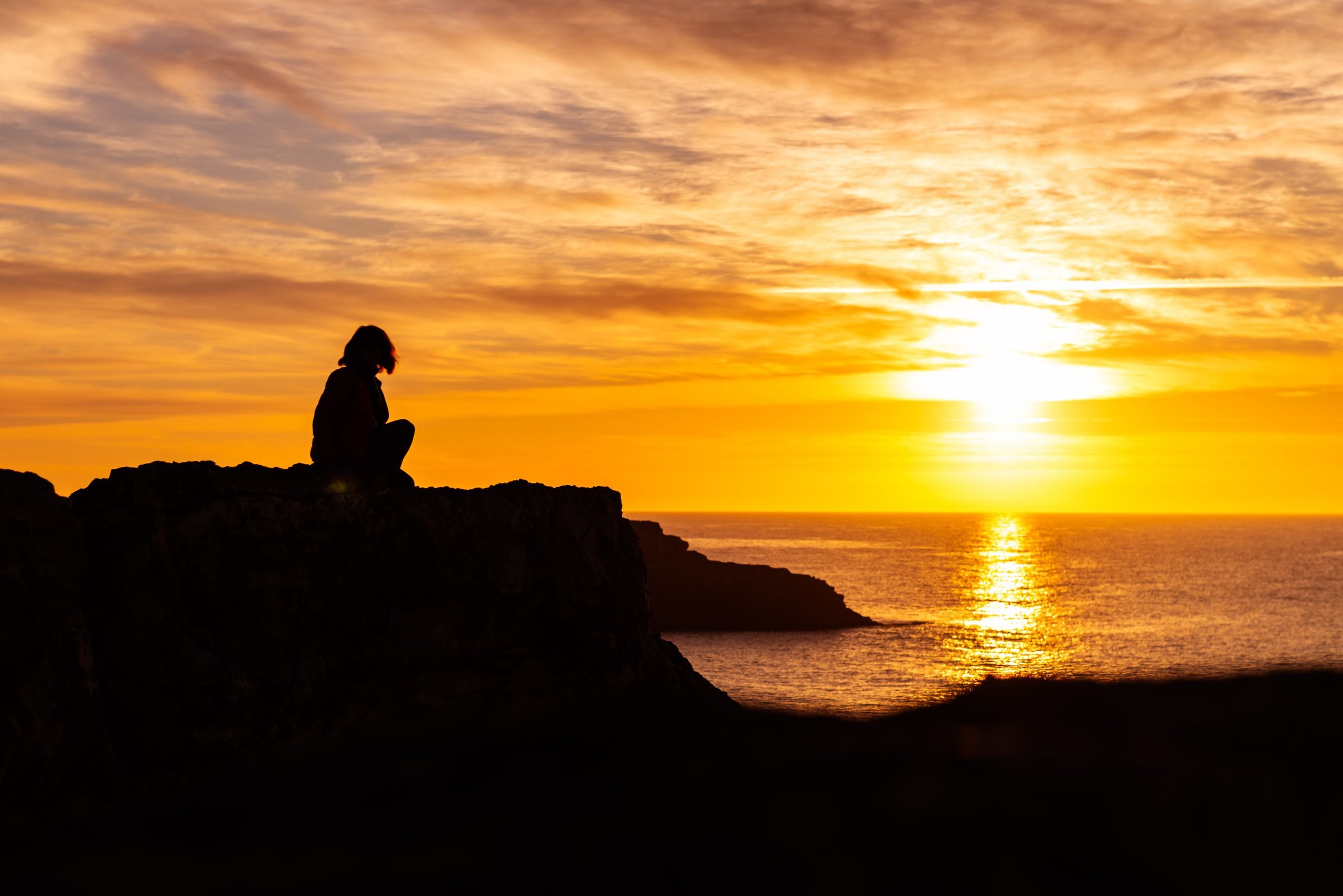 Silhouette of young woman on the edge of the cliff with sea view during sunrise. Holidays and enjoying life concept