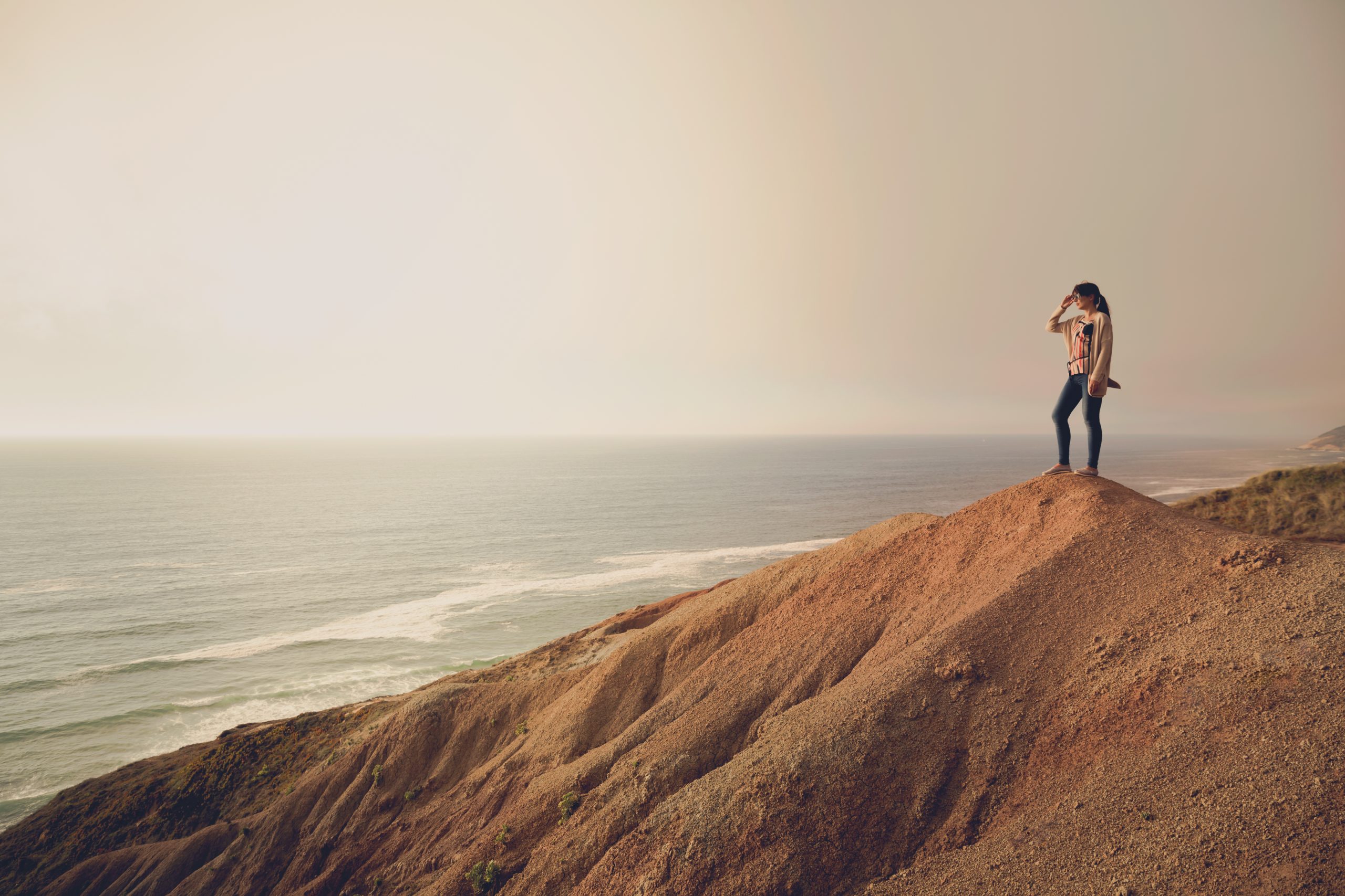 Woman on the top of a clif looking to the ocean