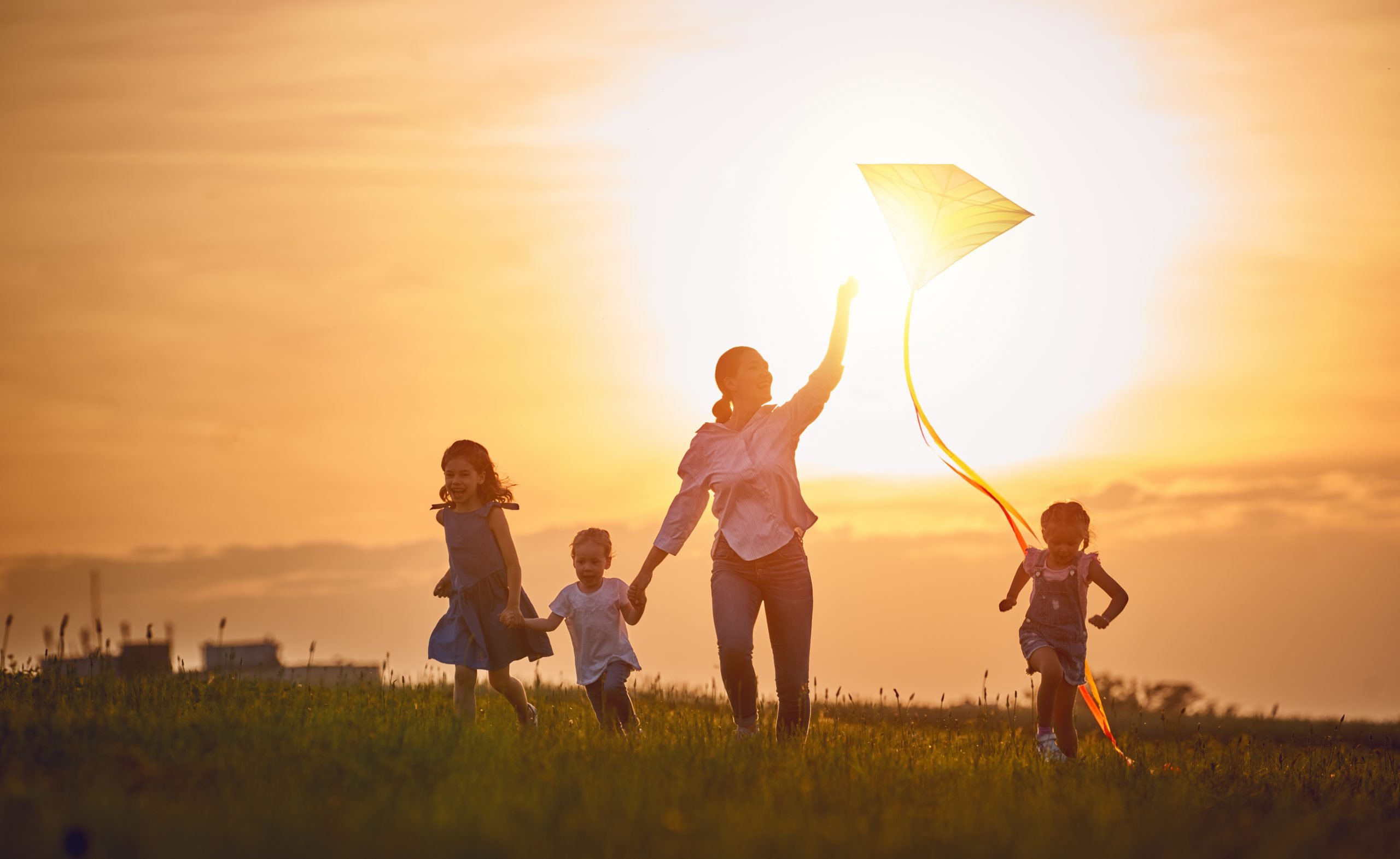 Happy family playing outdoor. Mother and children running on meadow with a kite in the summer on the nature.