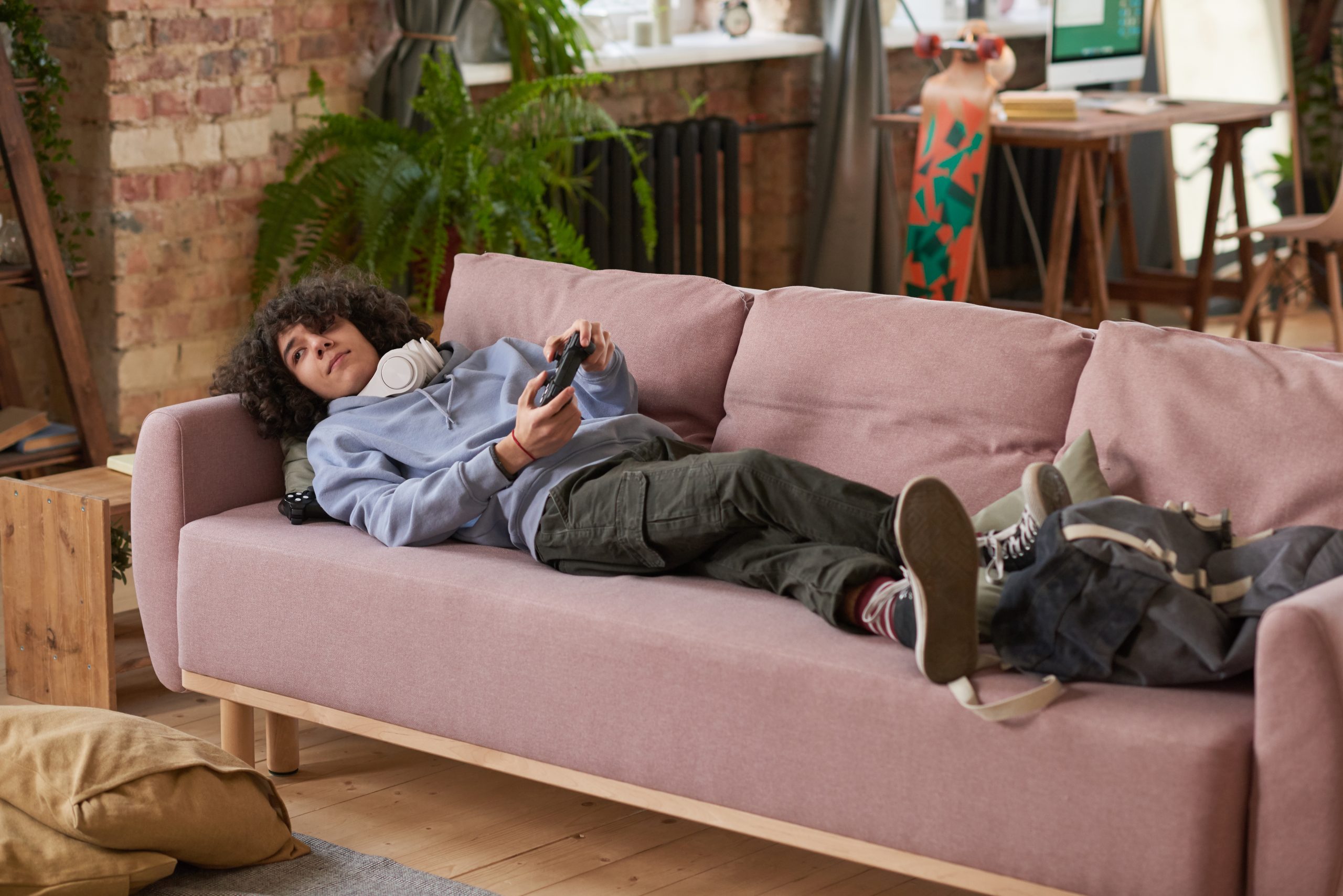 Guy lying on the sofa with joystick and playing video game during his leisure time in the room