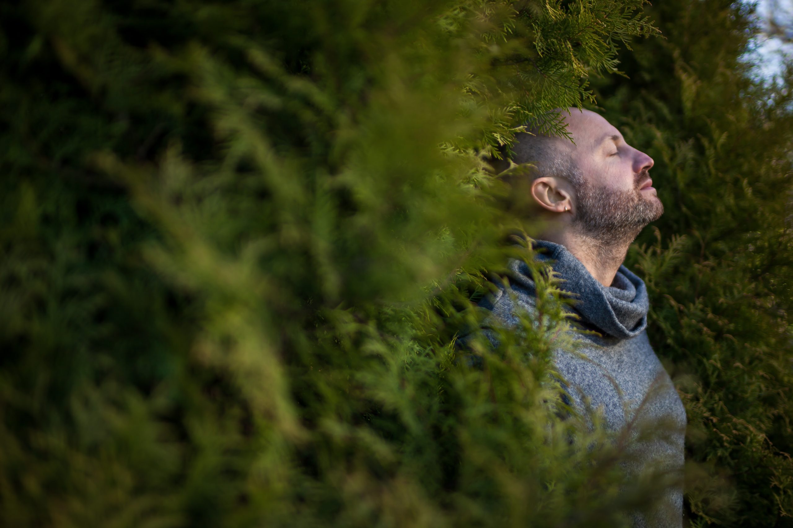 A bald man in a warm sweater is resting, leaning against the trees. Breathe fresh air in nature.