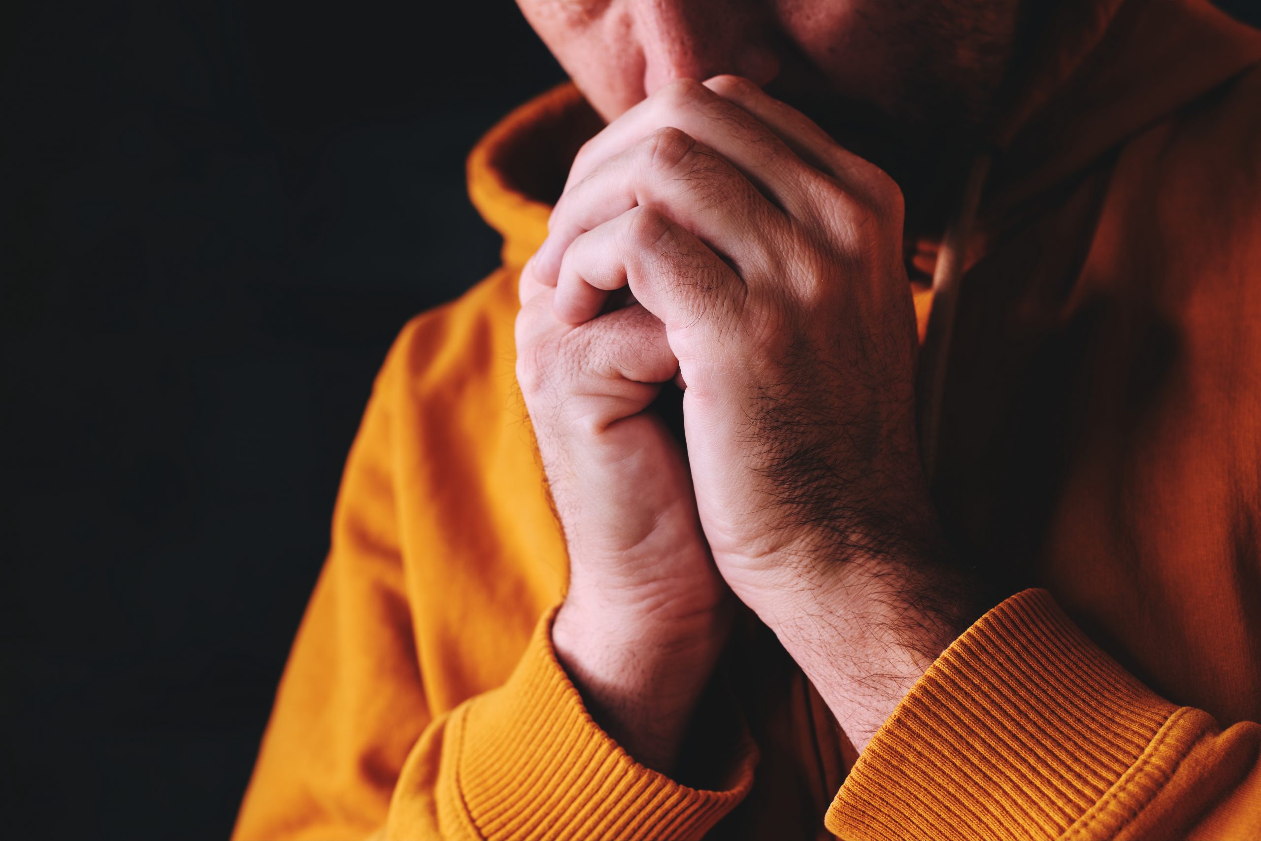 Christian man praying to God in dark room with clasped hands, close up with selective focus