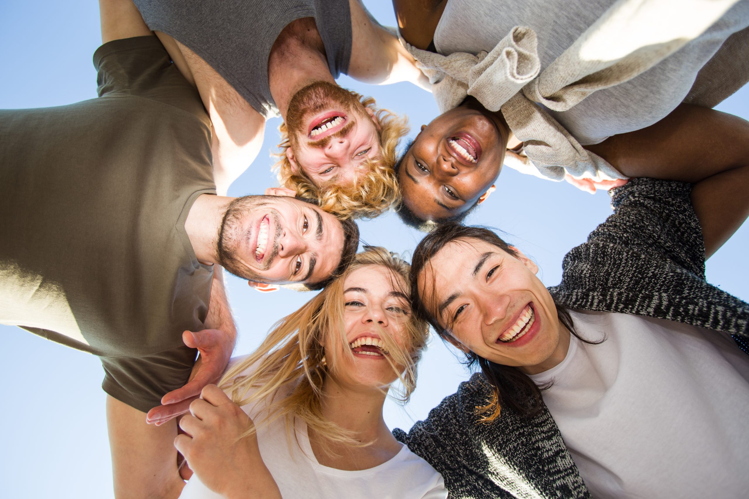 Cheerful friends huddling against blue sky on sunny day