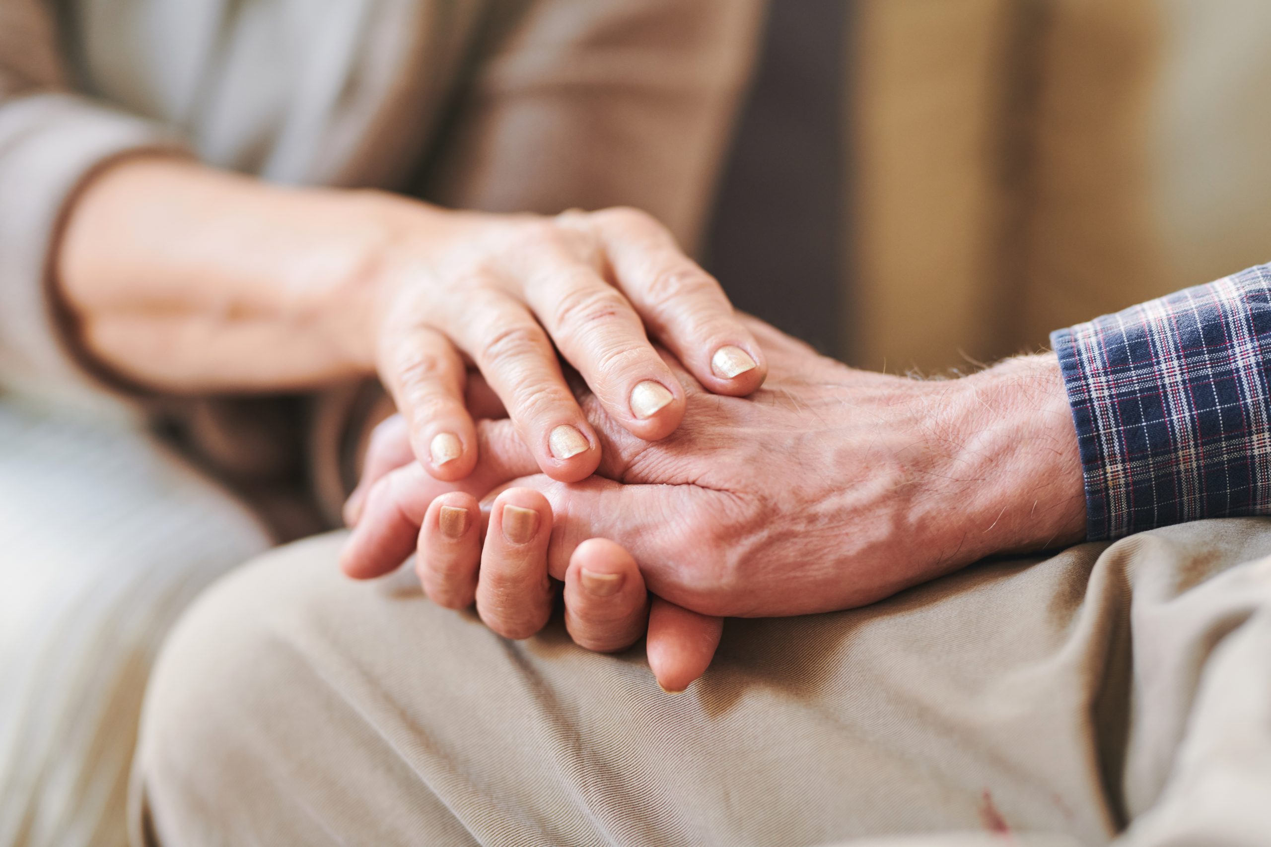 Senior male han between those of his mature wife or caregiver as symbol of support, care and love