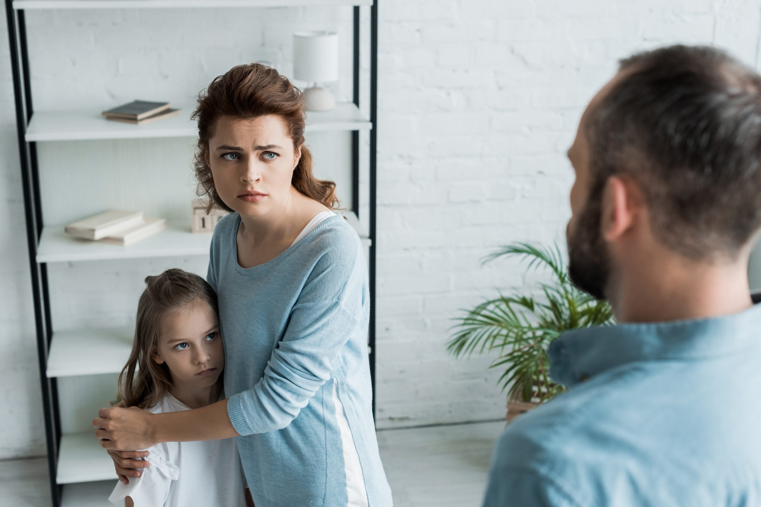 selective focus of scared mother hugging daughter and looking at husband