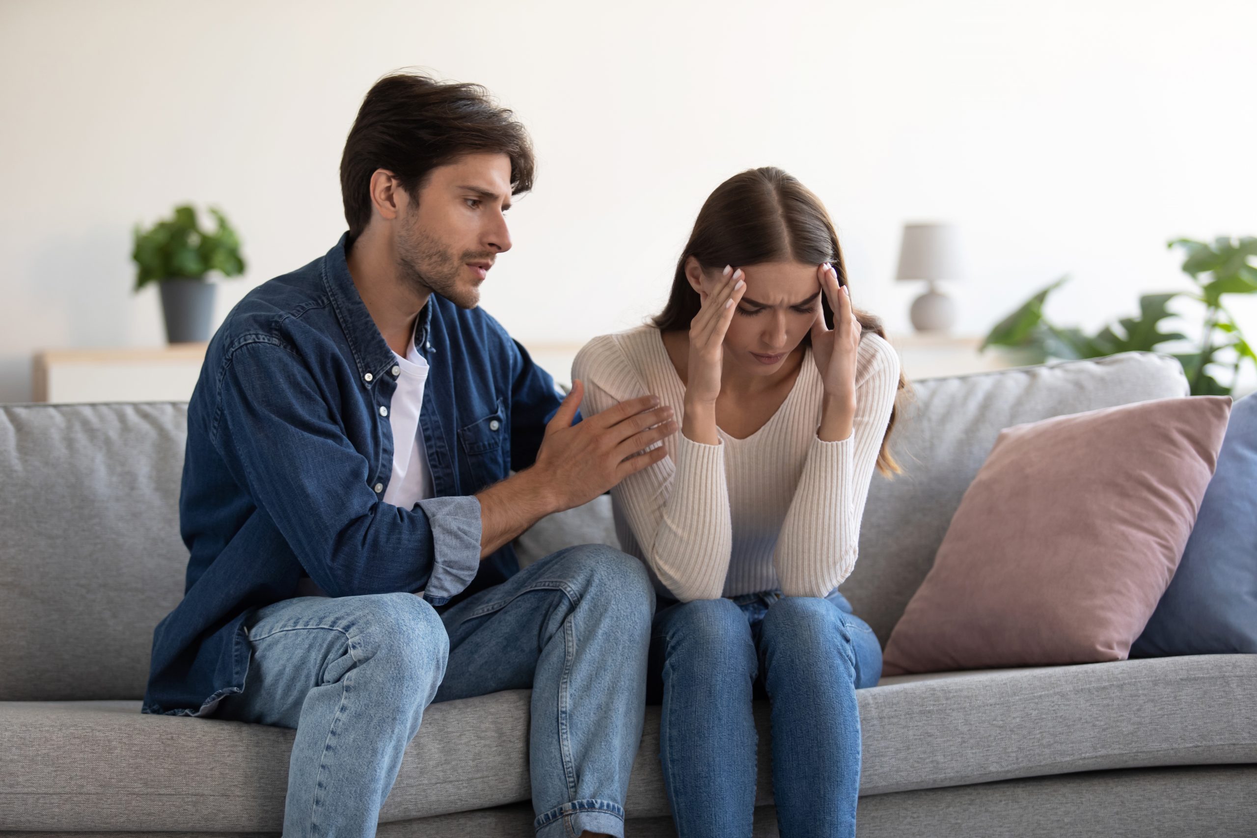 Young caucasian couple sit on sofa, husband calms upset wife at home interior. Loving man caresses lady, caring guy will conquer and make peace with his lover, show support, family overcome problems