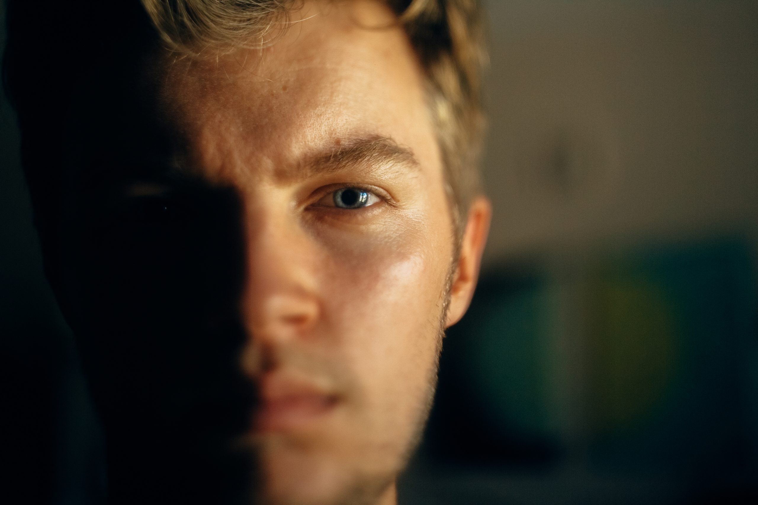 Serious man portrait in light on dark background. Closeup of man face with blue eyes and blonde hair in softlight. Selective focus. Creative image