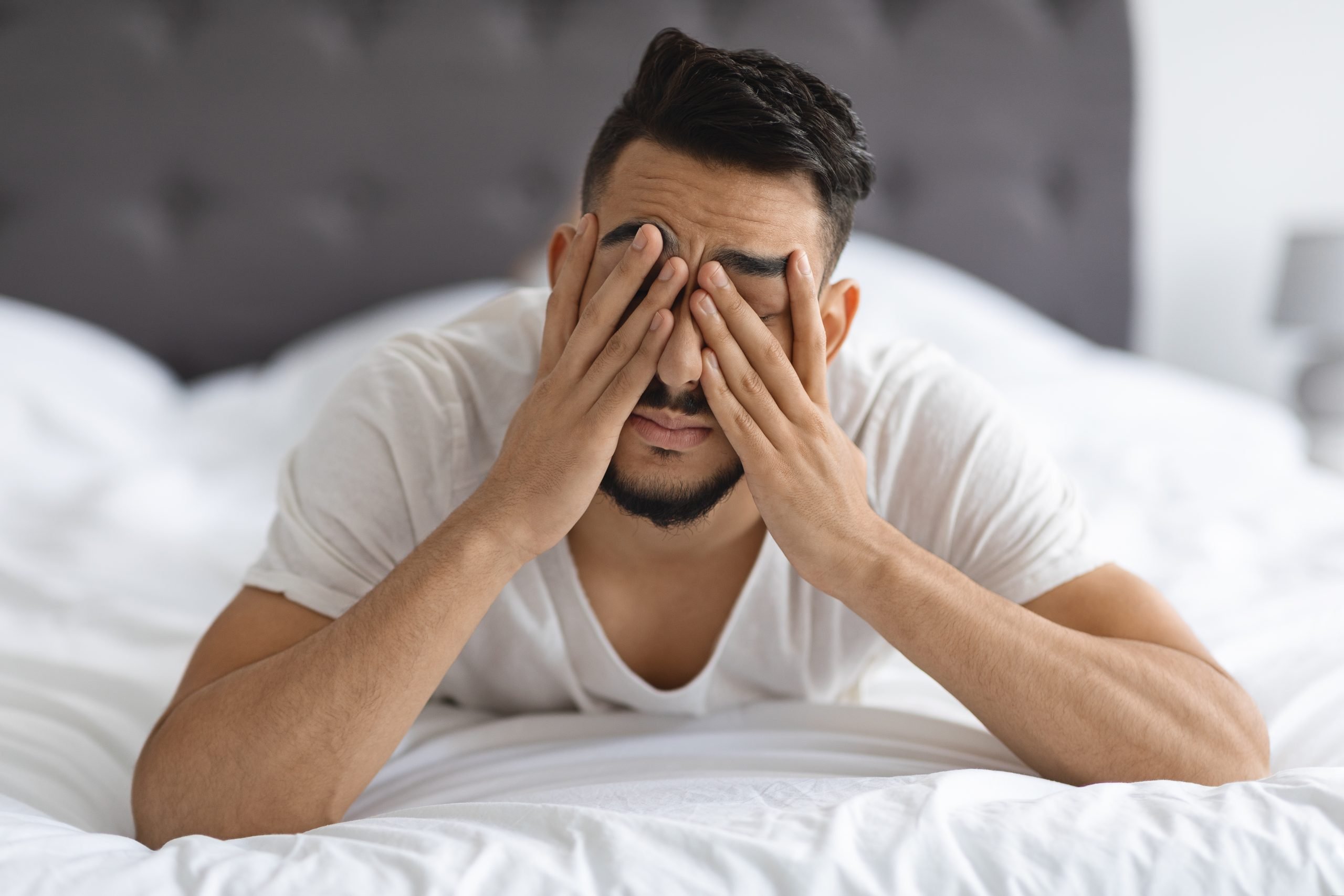 Young Arab Man Waking Up In Bed, Rubbing Eyes After Sleepless Night, Stressed Middle Eastern Guy Suffering From Insomnia Or Headache While Lying In Bedroom At Home, Closeup Shot With Free Space