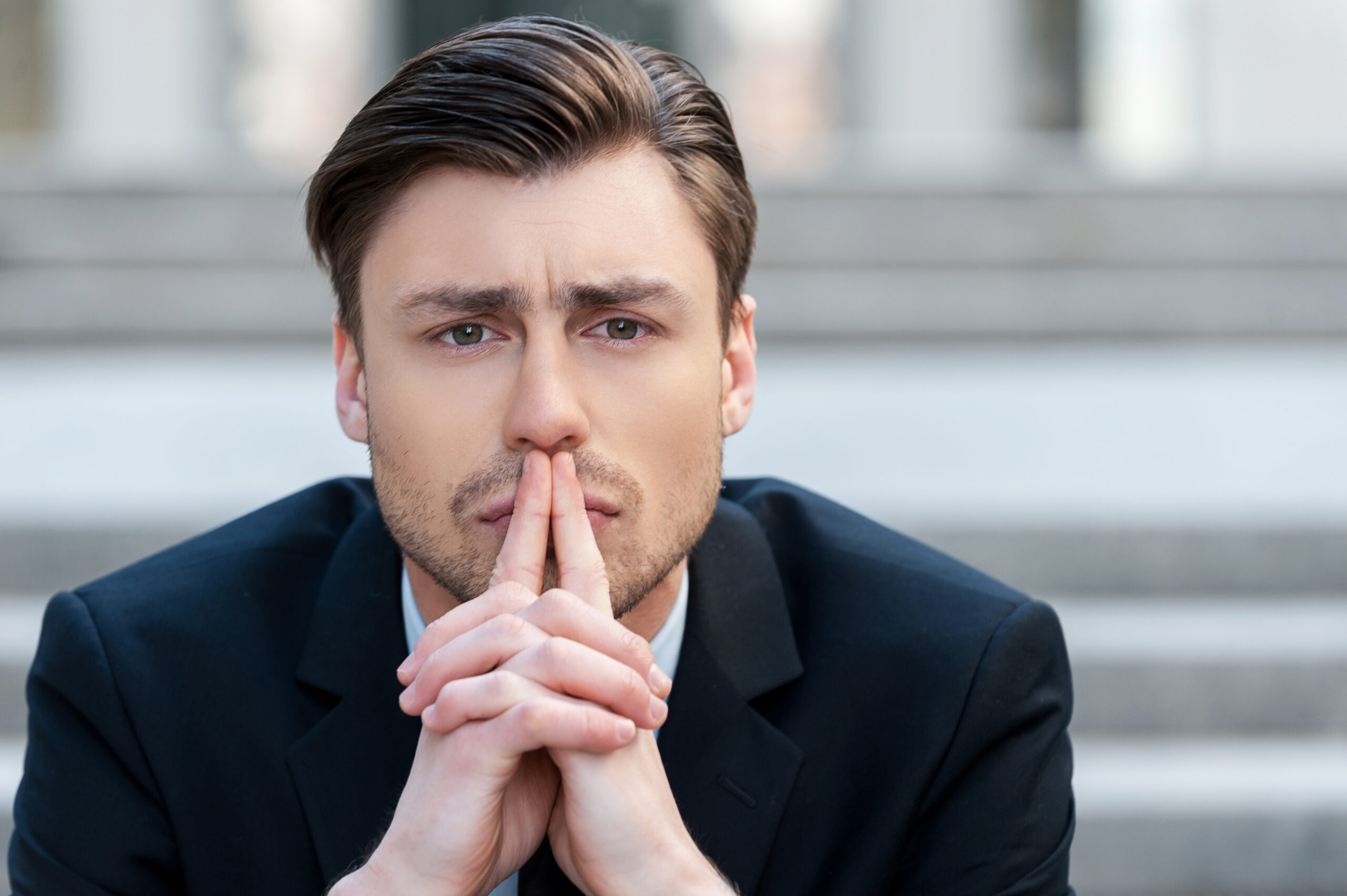 Thinking about solutions. Portrait of  young man in formalwear holding hands clasped and looking away while sitting outdoors