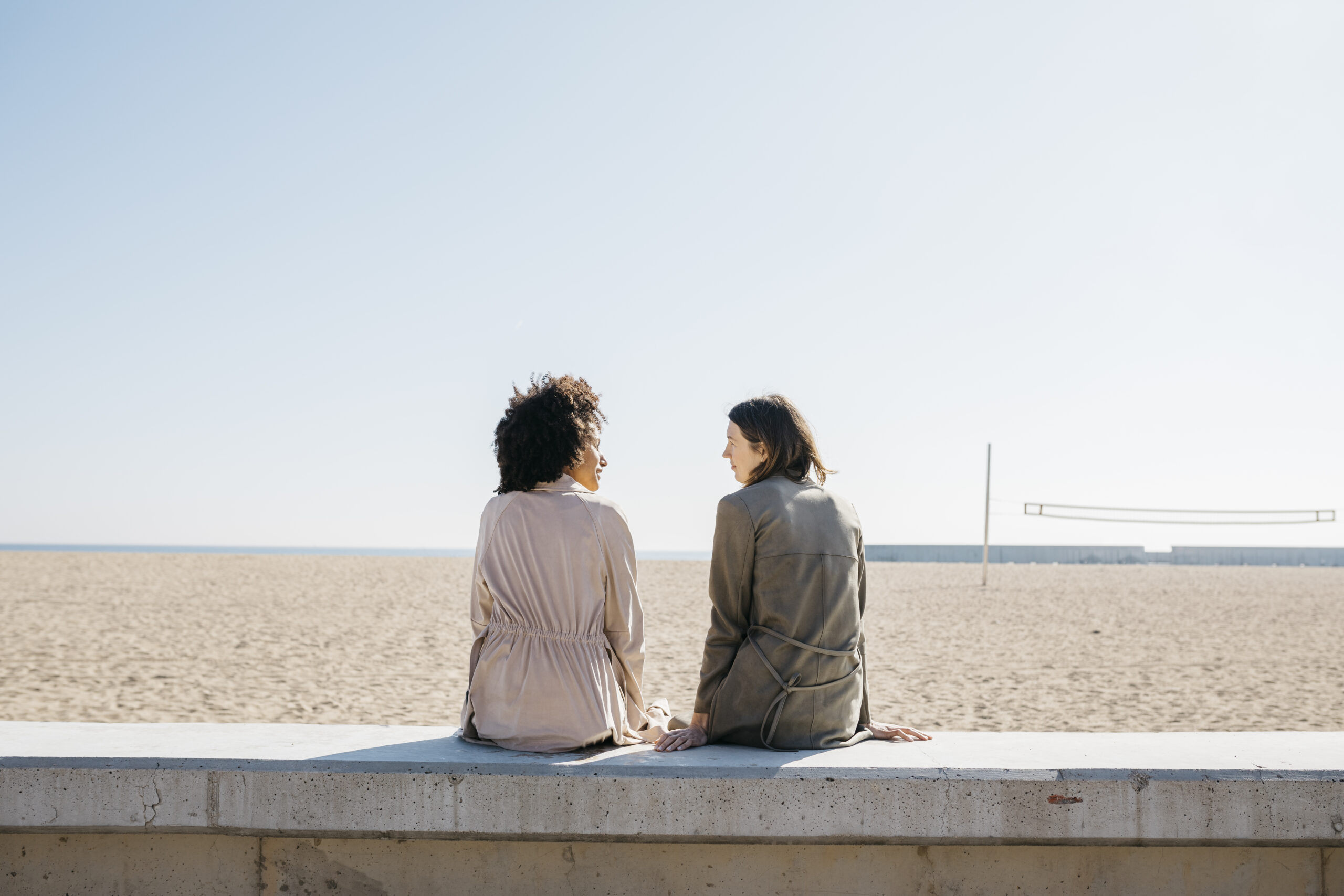 Back view of two friends sitting on the promenade enjoying leisure time