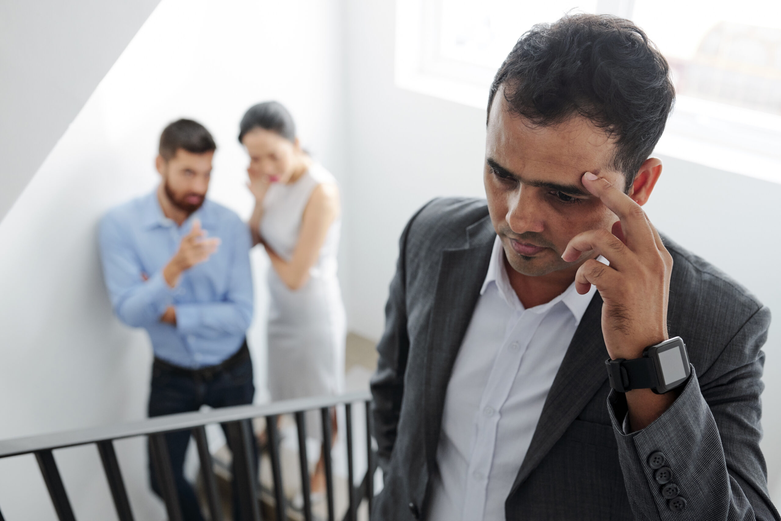 Businessman tired of hearing gossips behind his back, he is walking up the stairs and eavesdropping on conversation of colleagues