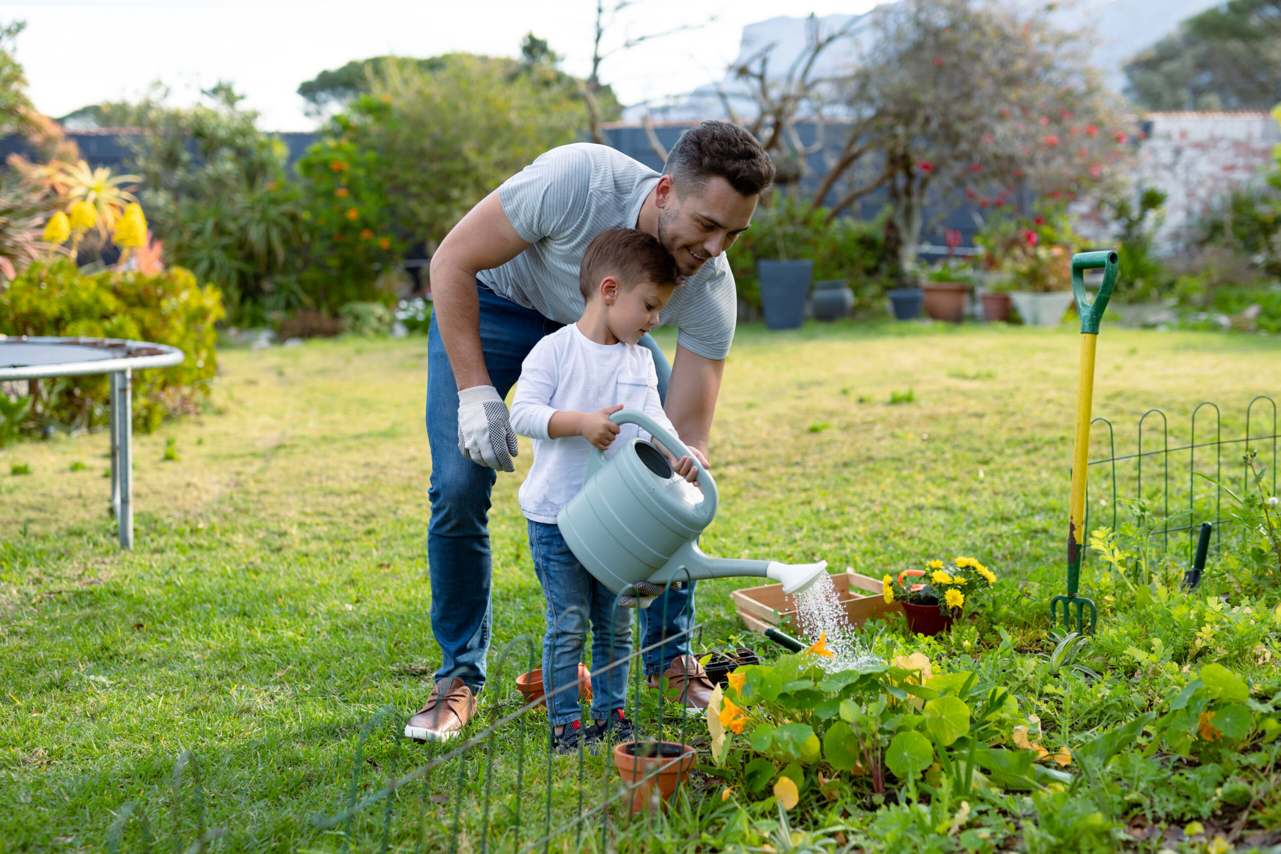 Happy caucasian father and son watering plants together. family time, having fun together at home and garden.