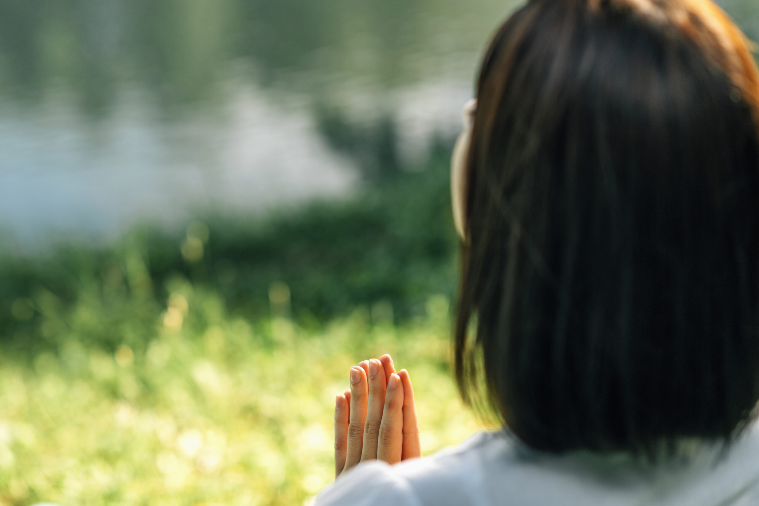Mindful Young woman, feeling grateful, meditating, sitting by the water, hands in prayer position