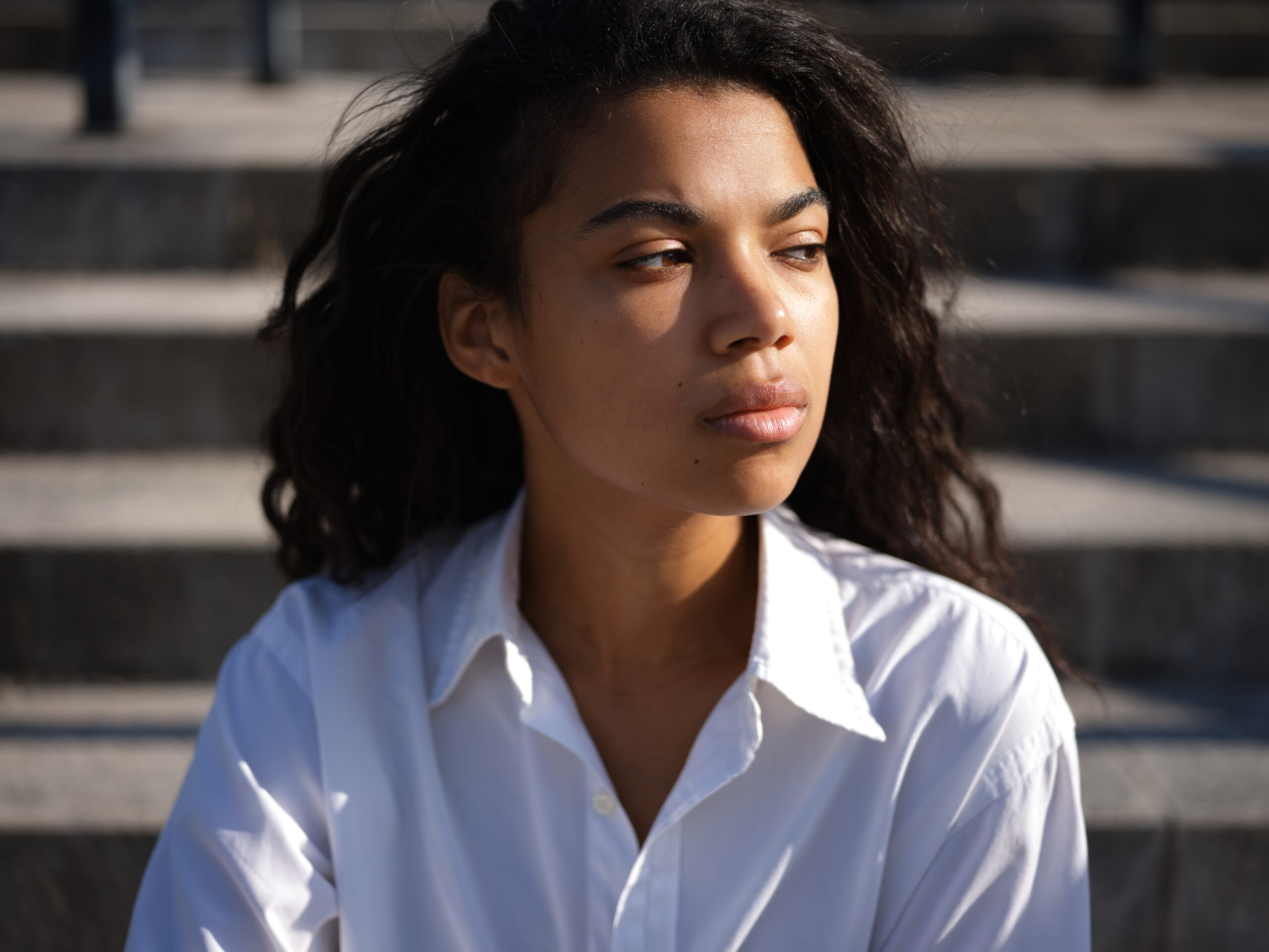 Resentment. Portrait of beautiful young mixed race woman in casual white shirt looking thoughtful aside while posing outdoors on a warm sunny day. Selective focus. Medium format shot