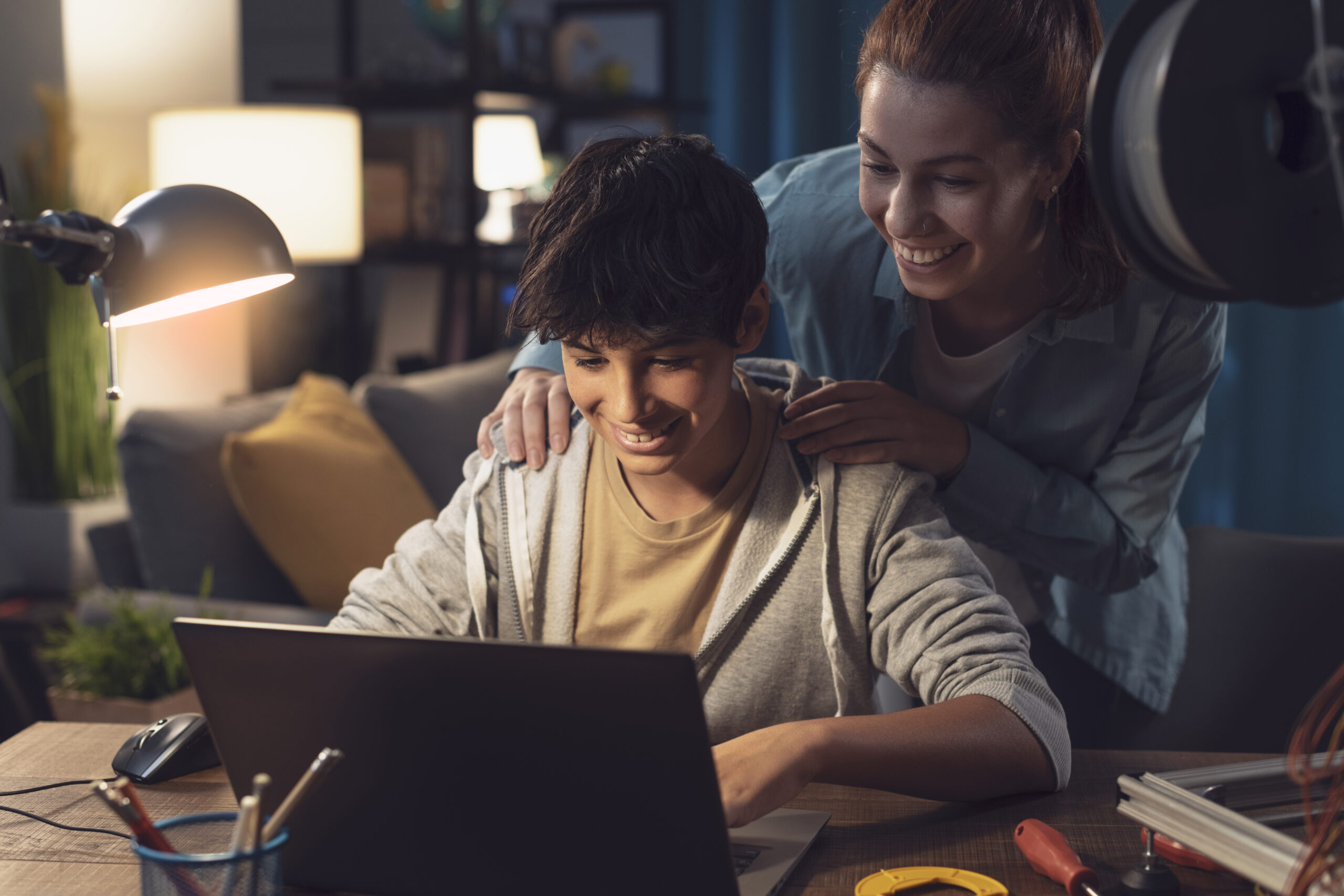 Teenagers learning 3D modeling and using a 3D printer, the boy is using a laptop and the girl is helping him