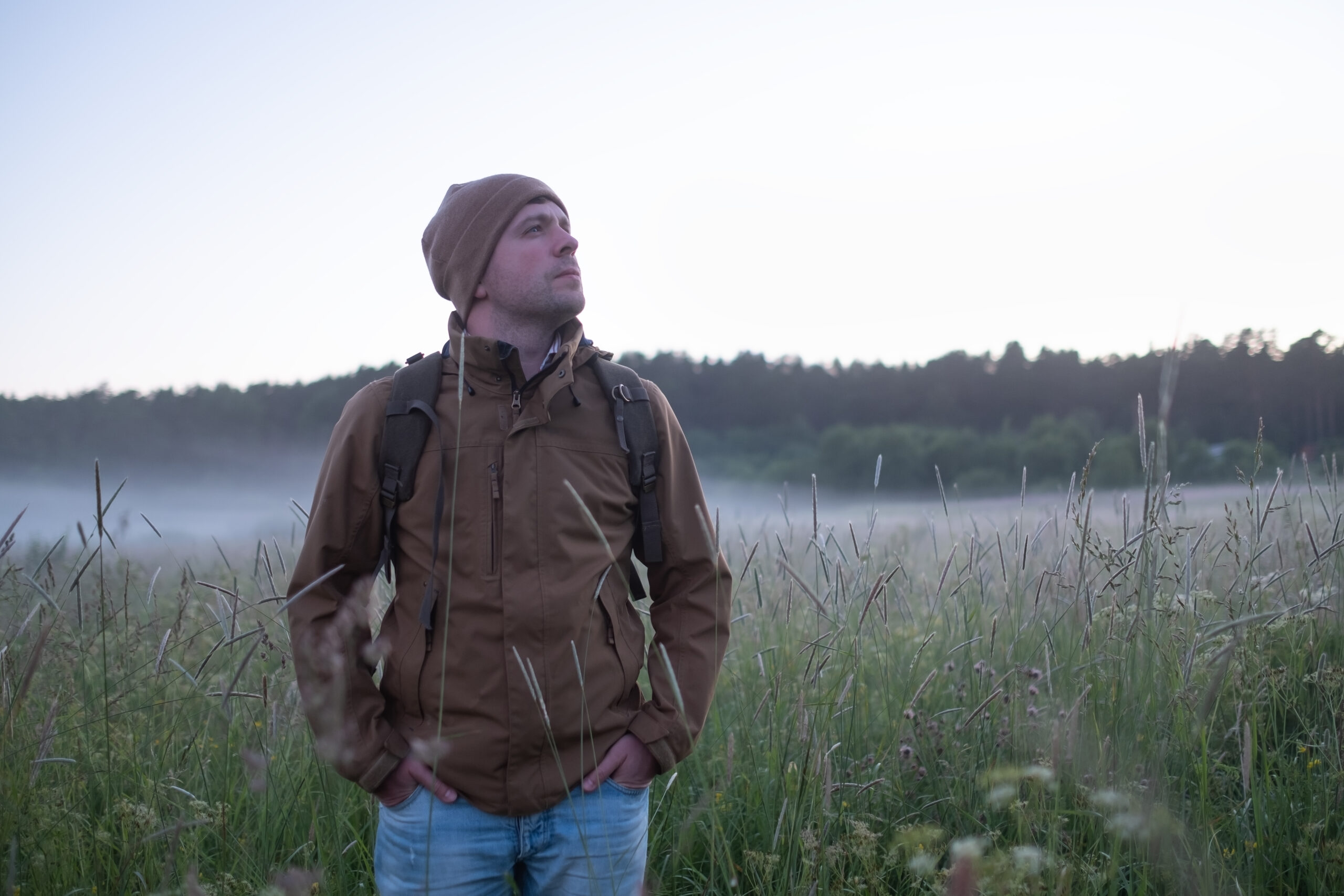 Mature backpacker walking in summer meadow at the evening