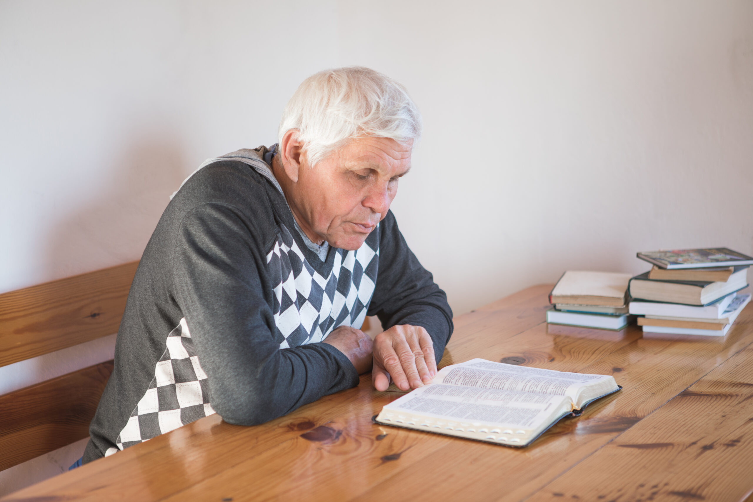 senior man praying, reading an old Bible. Hands folded in prayer on a Holy Bible in church concept for faith, spirituality and religion