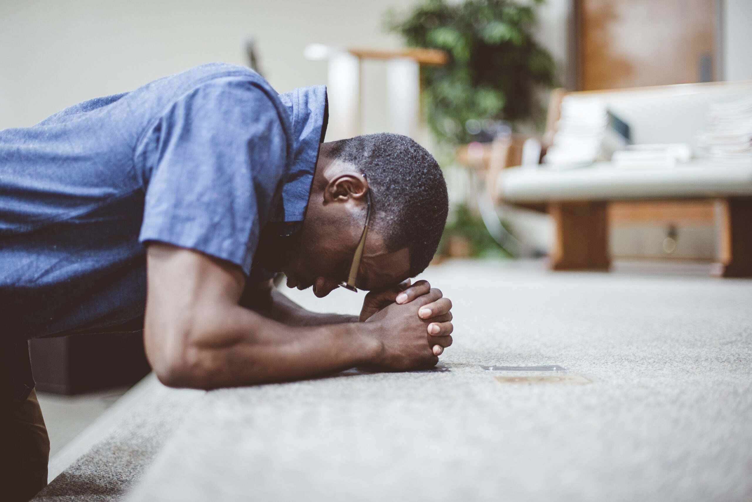 An African-American male praying on his knees with his head down at the church