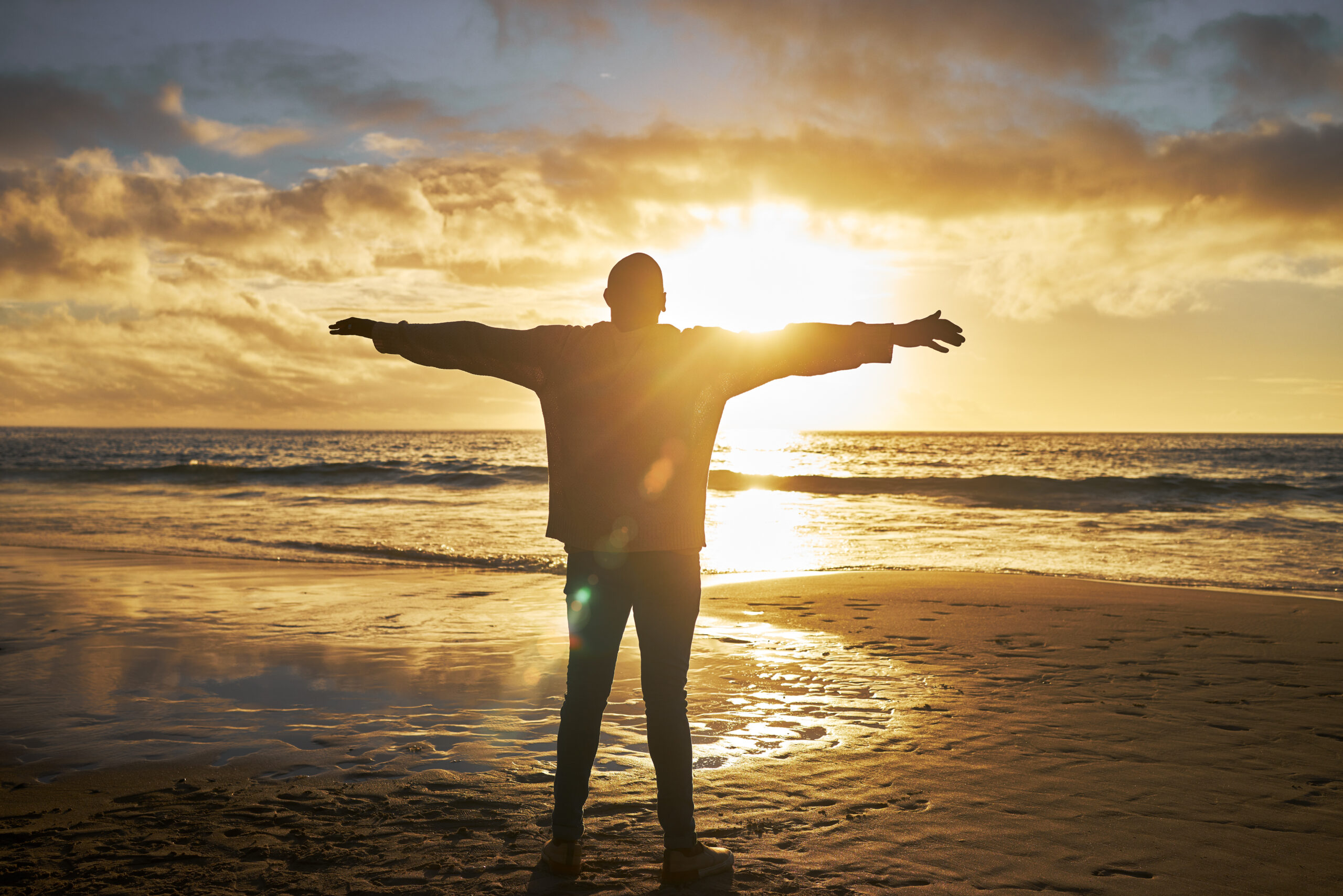 Worship, sunrise and silhouette of man at the beach standing with arms raised. Faith, religious and.