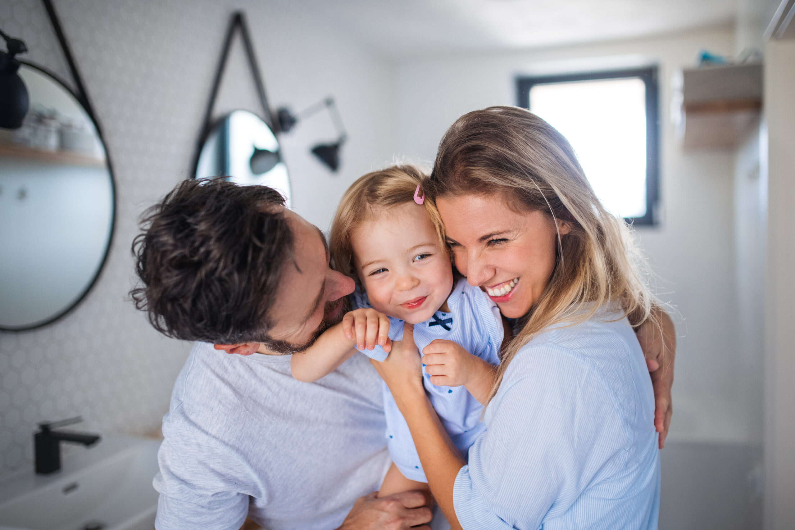 A young family with small daughter indoors in bathroom, hugging.