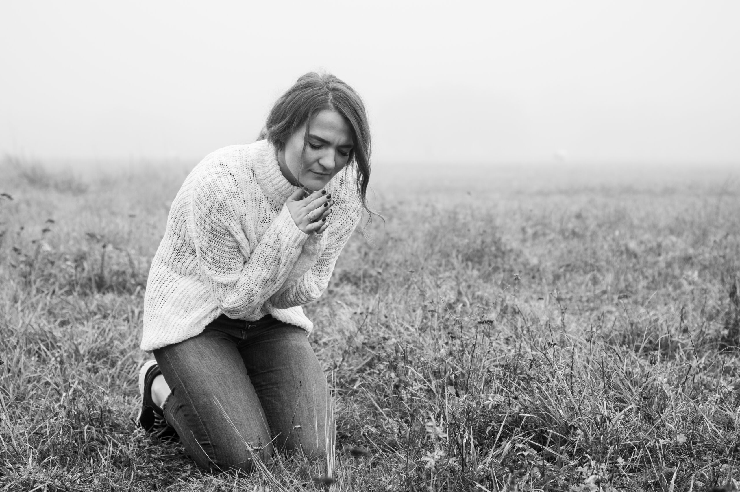 Girl closed her eyes, praying in a field during beautiful fog. Hands folded in prayer concept for faith, spirituality and religion. Peace, hope, dreams concept