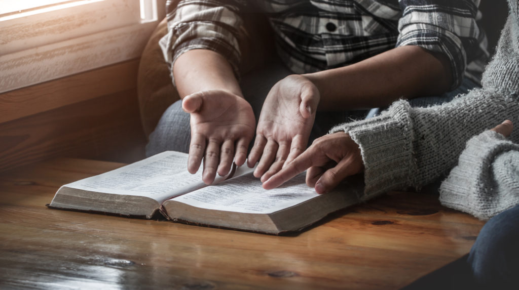 Two christianity sitting around wooden table with open holy bible and reading.