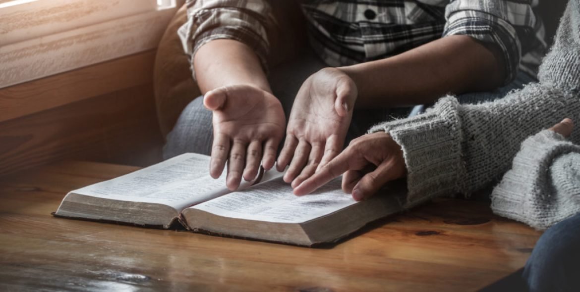 Two christianity sitting around wooden table with open holy bible and reading.