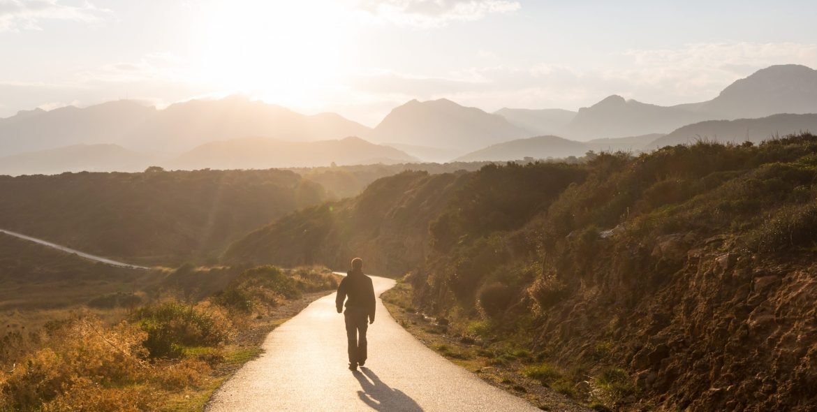 Scenic road in the mountains. Travel background. Man going on sunrise background.