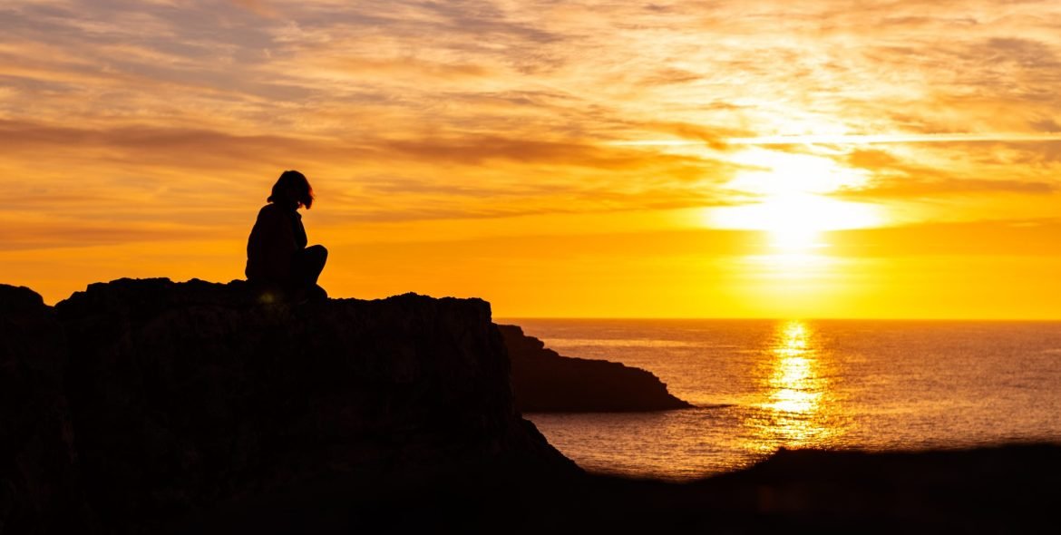 Silhouette of young woman on the edge of the cliff with sea view during sunrise. Holidays and enjoying life concept