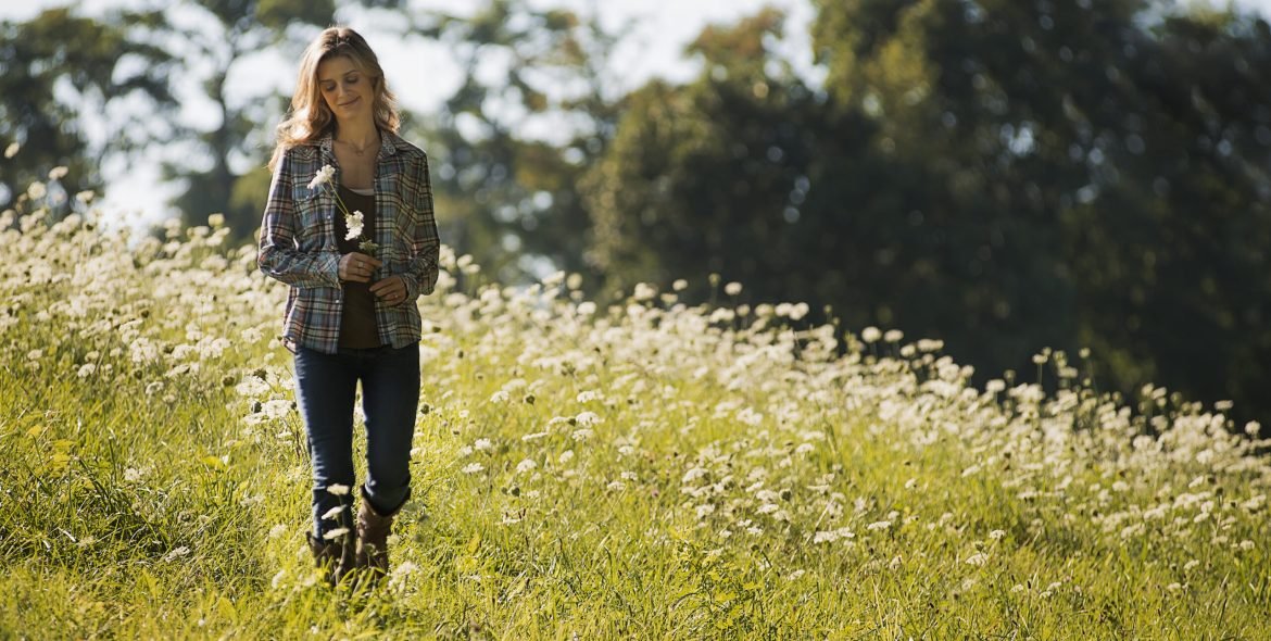 A young woman walking in a wild flower meadow.