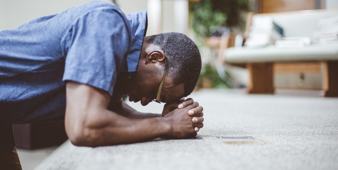 An African-American male praying on his knees with his head down at the church