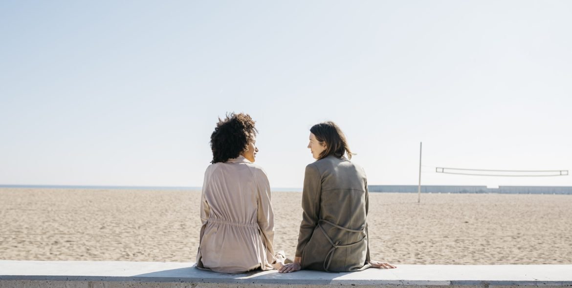 Back view of two friends sitting on the promenade enjoying leisure time