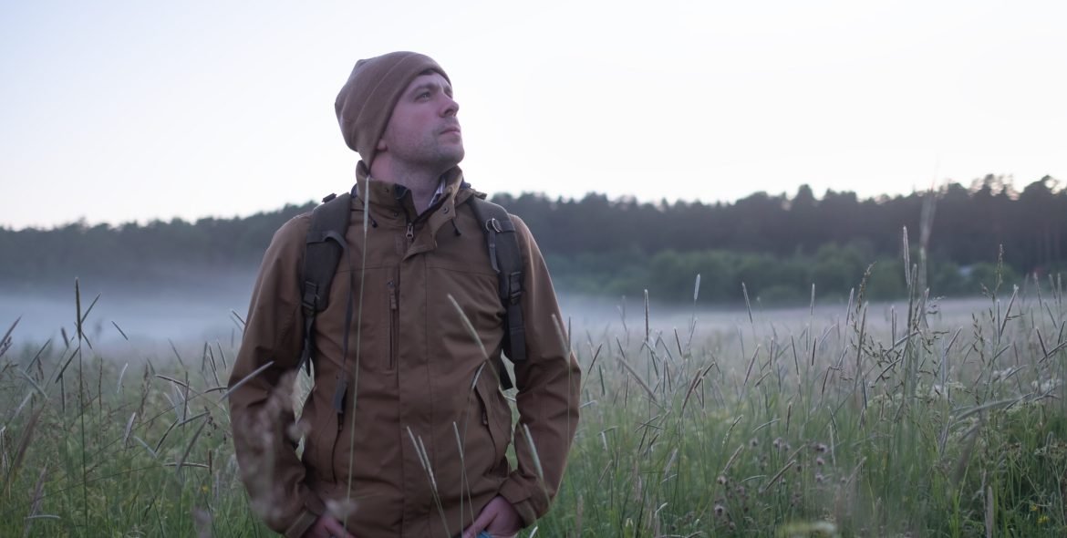 Mature backpacker walking in summer meadow at the evening