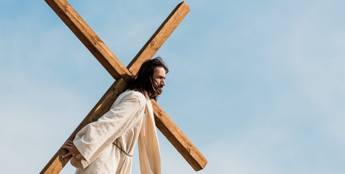 bearded jesus holding wooden cross against sky