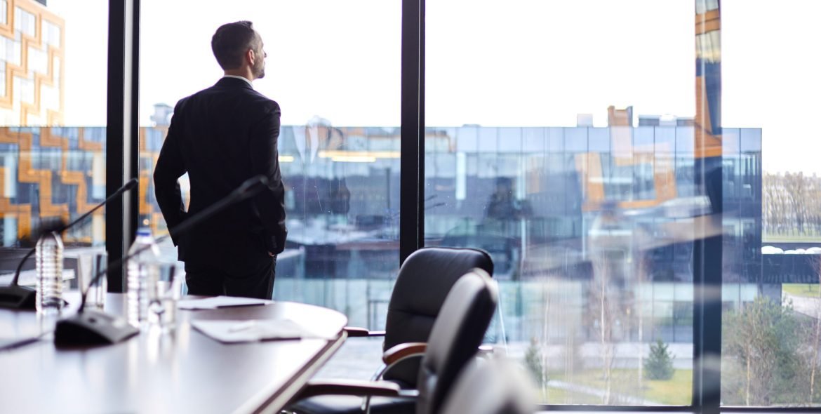 Elegant businessman in formalwear looking through large window in conference hall