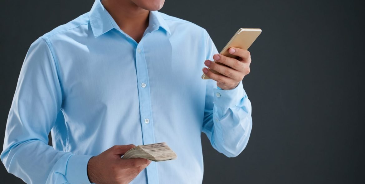 Cropped image of man with cash shopping via smartphone
