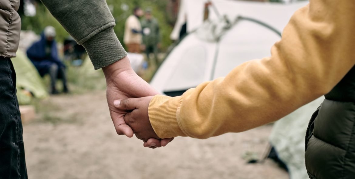 Rear view of unrecognizable children of different ages holding hands while coming in to migrant camp