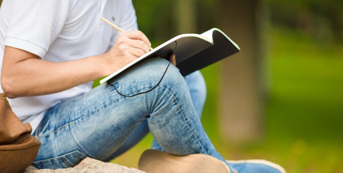Close-up of hands of boy studying for college exam in park outside