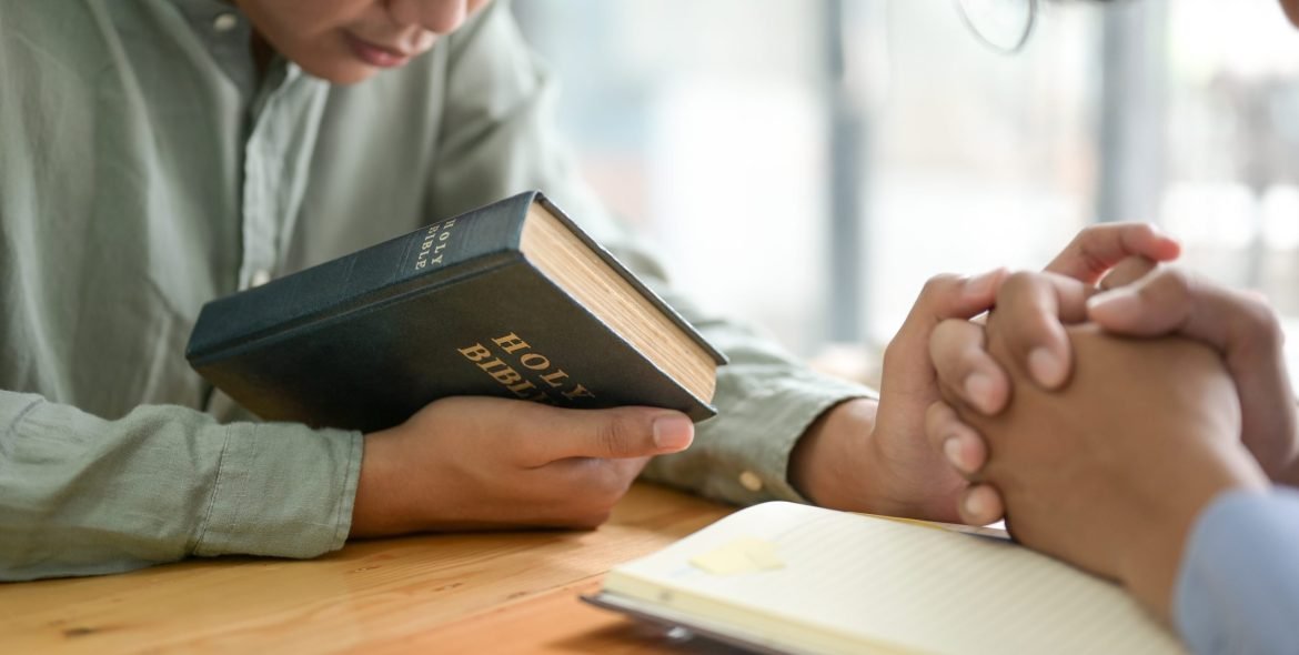 Close-up shot of The Bible and people praying.