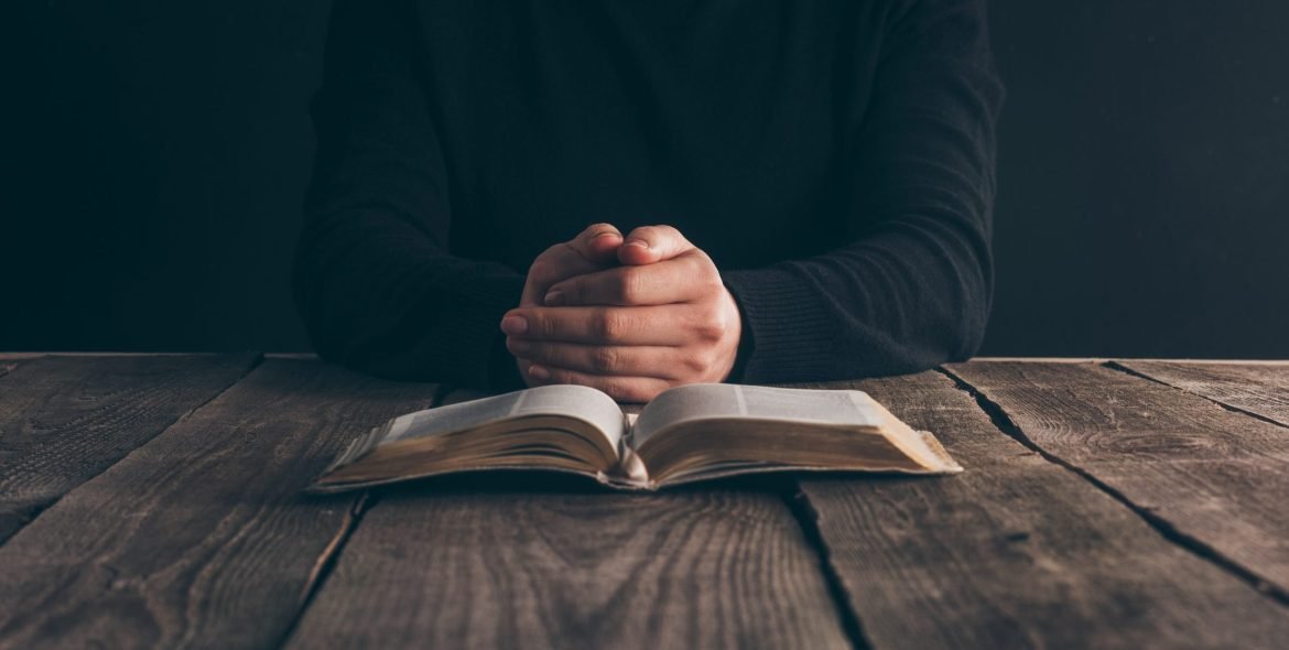 cropped image of nun sitting at table with bible and praying