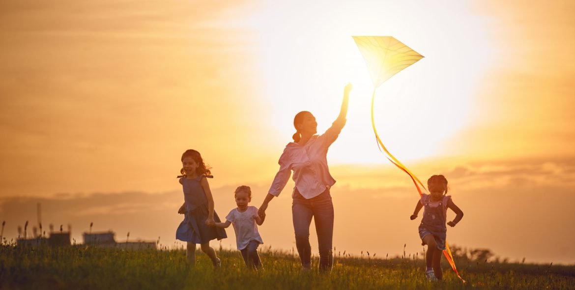 Happy family playing outdoor. Mother and children running on meadow with a kite in the summer on the nature.