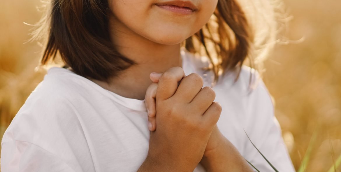 Little Girl closed her eyes, praying in a field wheat. Hands folded in prayer. Religion concept