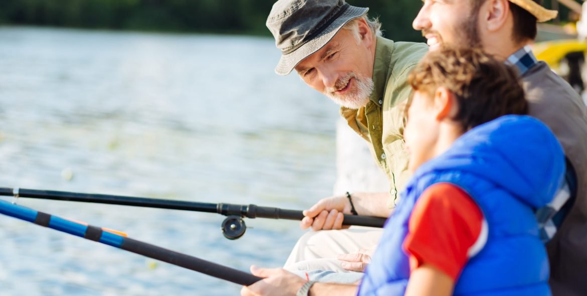 Bearded grey-haired grandfather talking to grandson while having family fishing