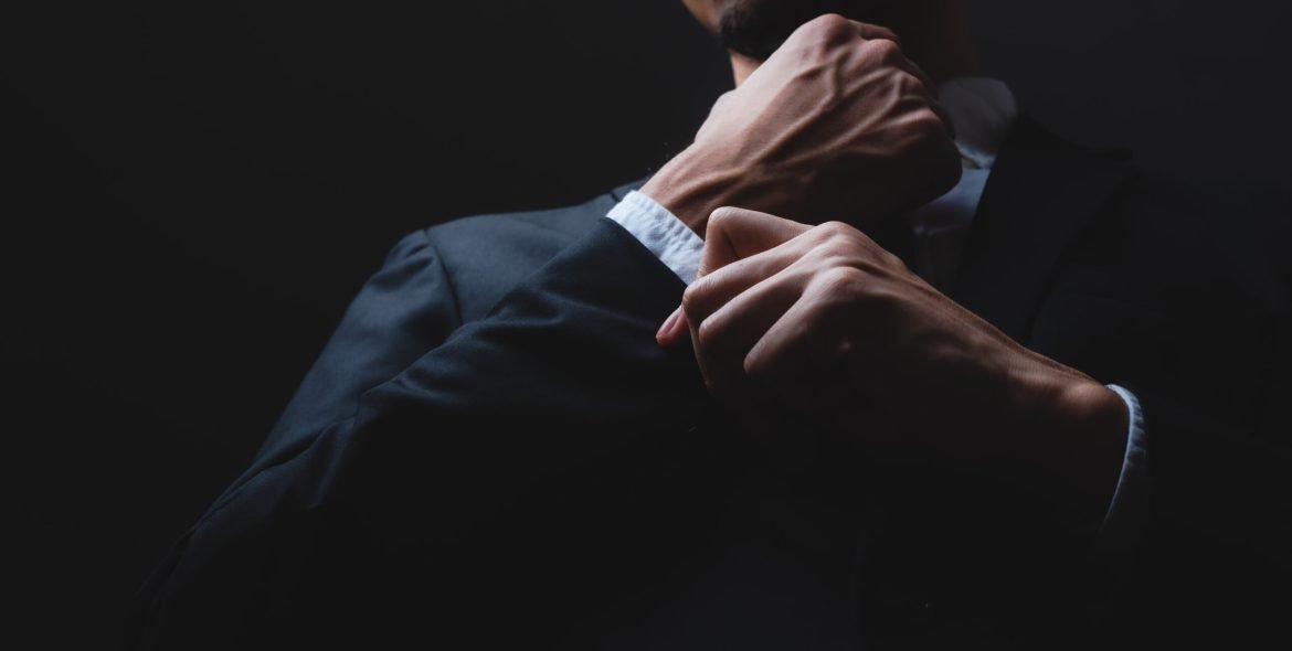 handsome confident businessman wearing and adjusting the black suit
