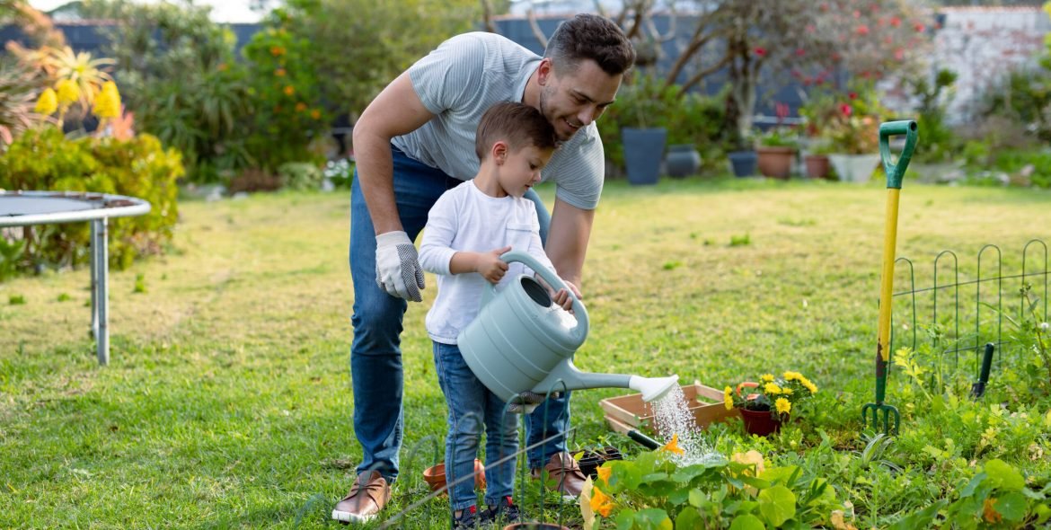 Happy caucasian father and son watering plants together. family time, having fun together at home and garden.