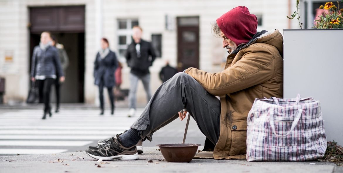 A homeless beggar man sitting outdoors in city asking for money donation. Copy space.