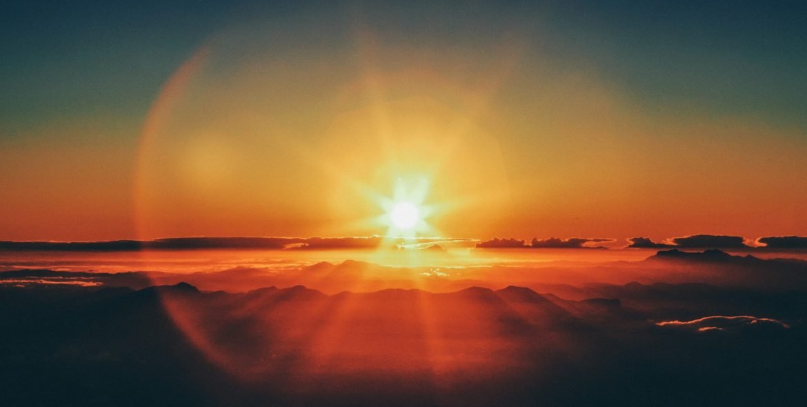 A horizontal shot of a sunset from a mountain cliff with the sun visible in the distance