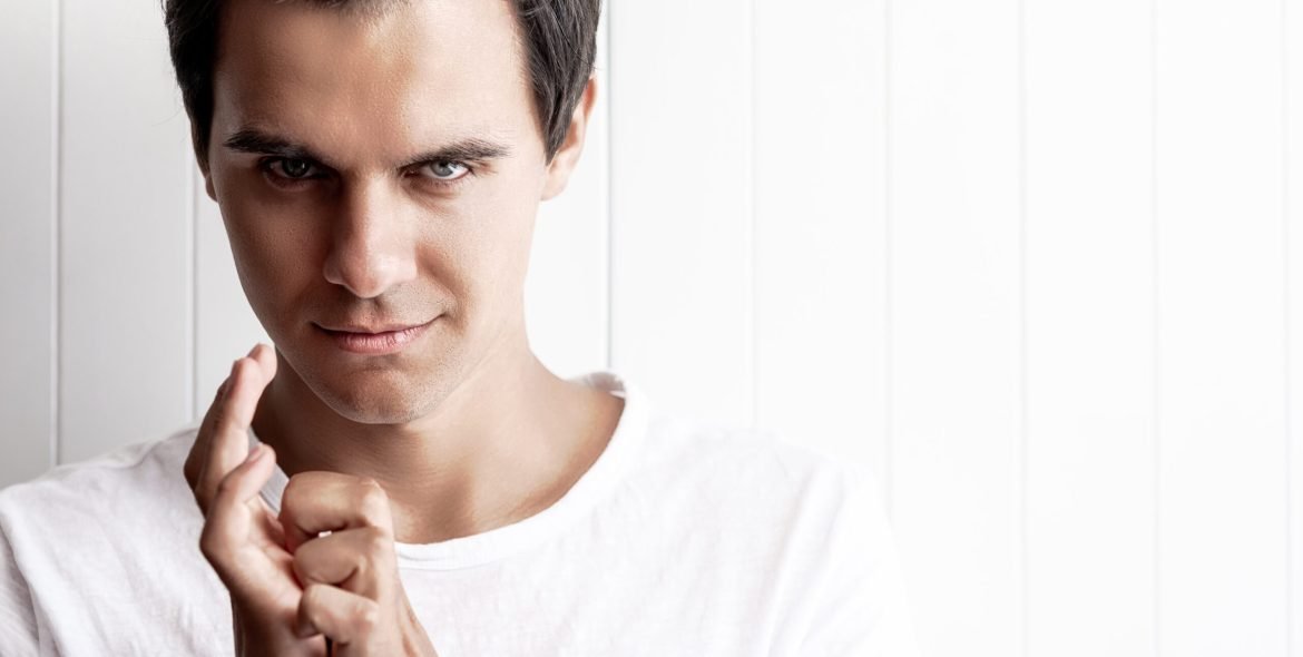 Young man holding hands together and looking at camera with thoughts of revenge and jealousy. Horizontal shot